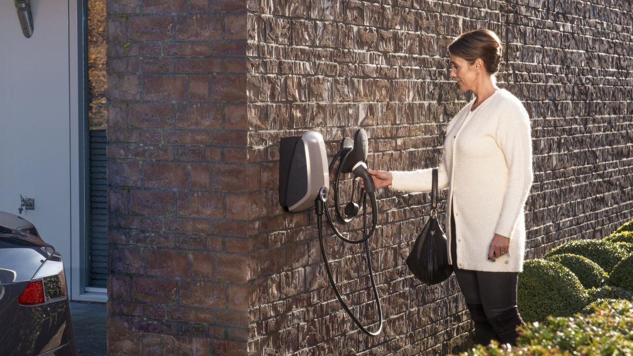 一位女士抓住了安装在她家墙壁上的 EVBox Elvi Home 充电器的连接线。