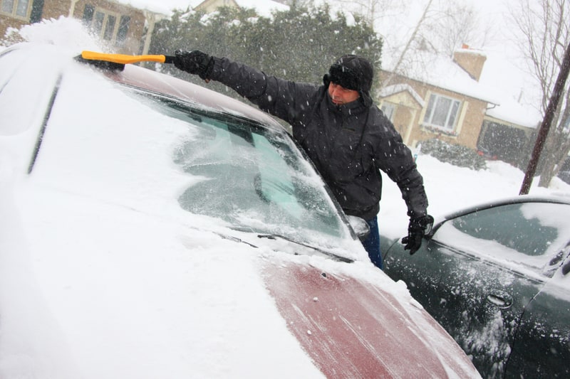 一个男人在暴风雪后用扫雪刷从车上扫雪 