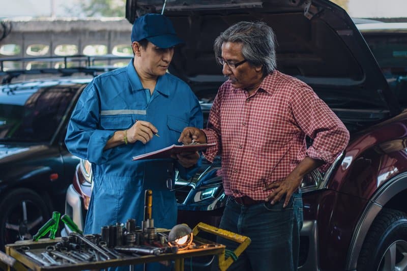 汽车修理工向一位年长客户解释要在汽车上完成的维护清单