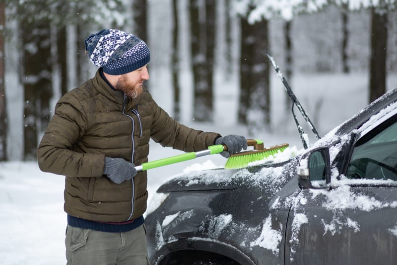 在冬日，男人用刷子从雪中清洗汽车