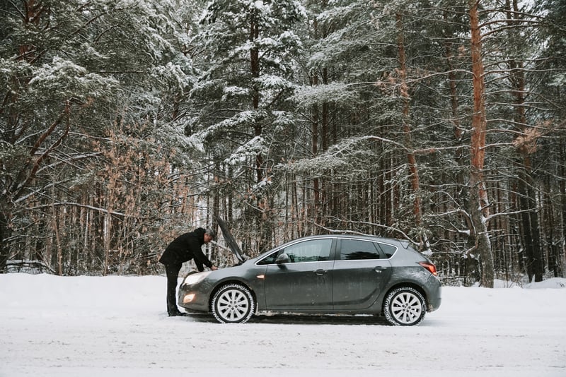 冬天，森林里有雪的男人检查引擎盖打开的死车